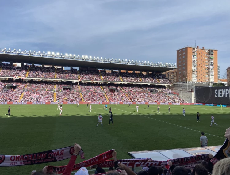 Estadio de Vallecas lleno durante un partido del Rayo, con un bloque de viviendas del barrio al fondo