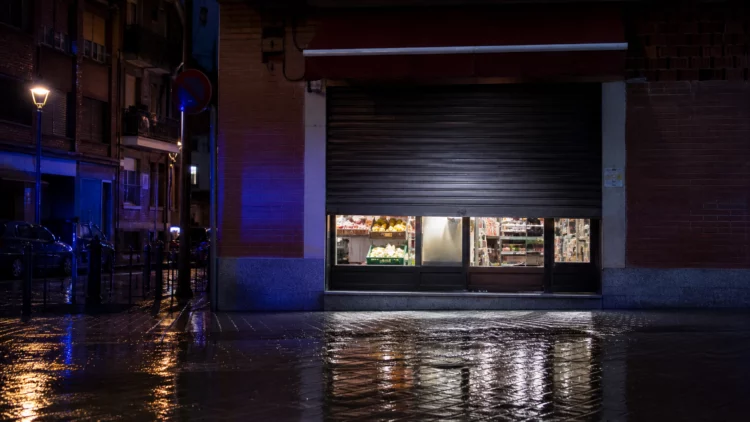 Comercio de alimentación de barrio con la persiana a medio cerrar y luces policiales reflejadas en la calle