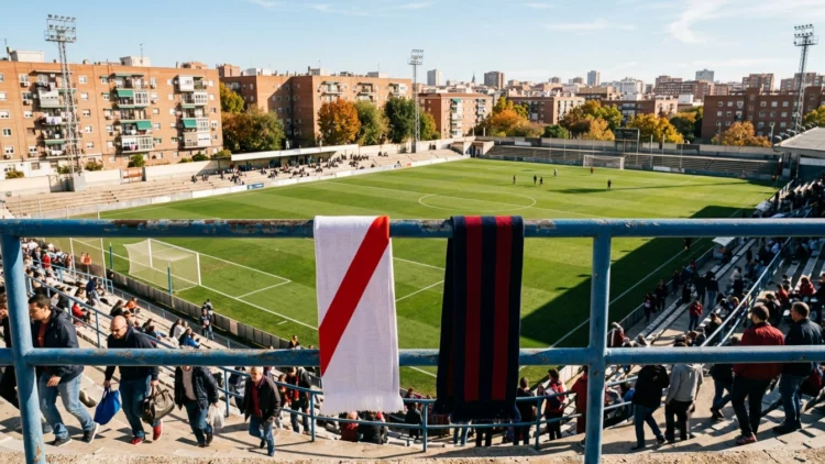 Bufandas con la franja roja del Rayo y los colores del Cagliari ante un campo de fútbol