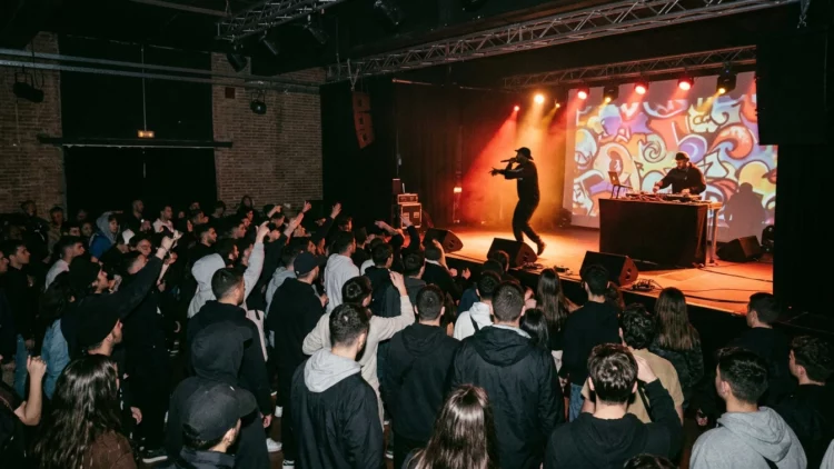 Concierto de hip hop en una sala con público y luces cálidas